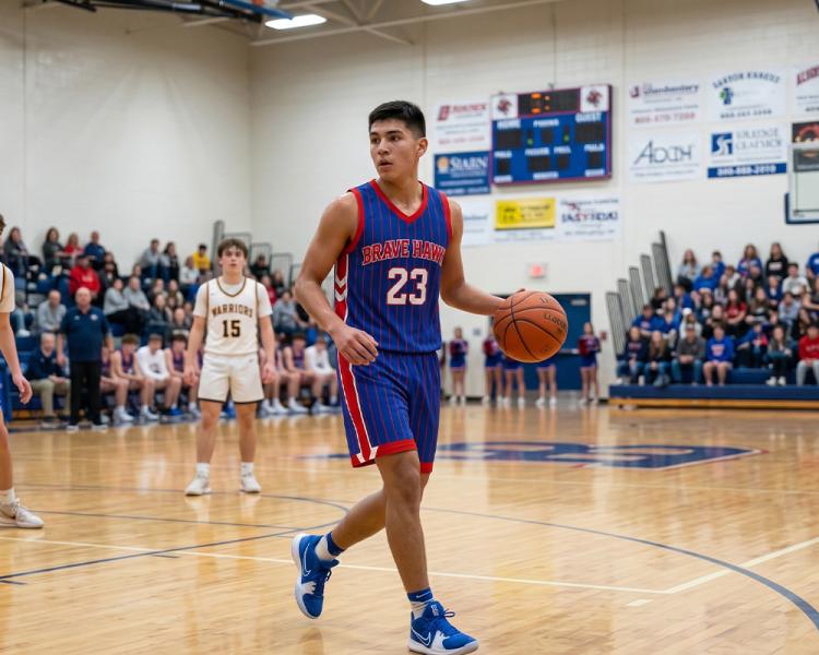 A high school basketball player wearing a blue uniform with red pinstripes and the number 23 dribbles a basketball down the court during an indoor game.